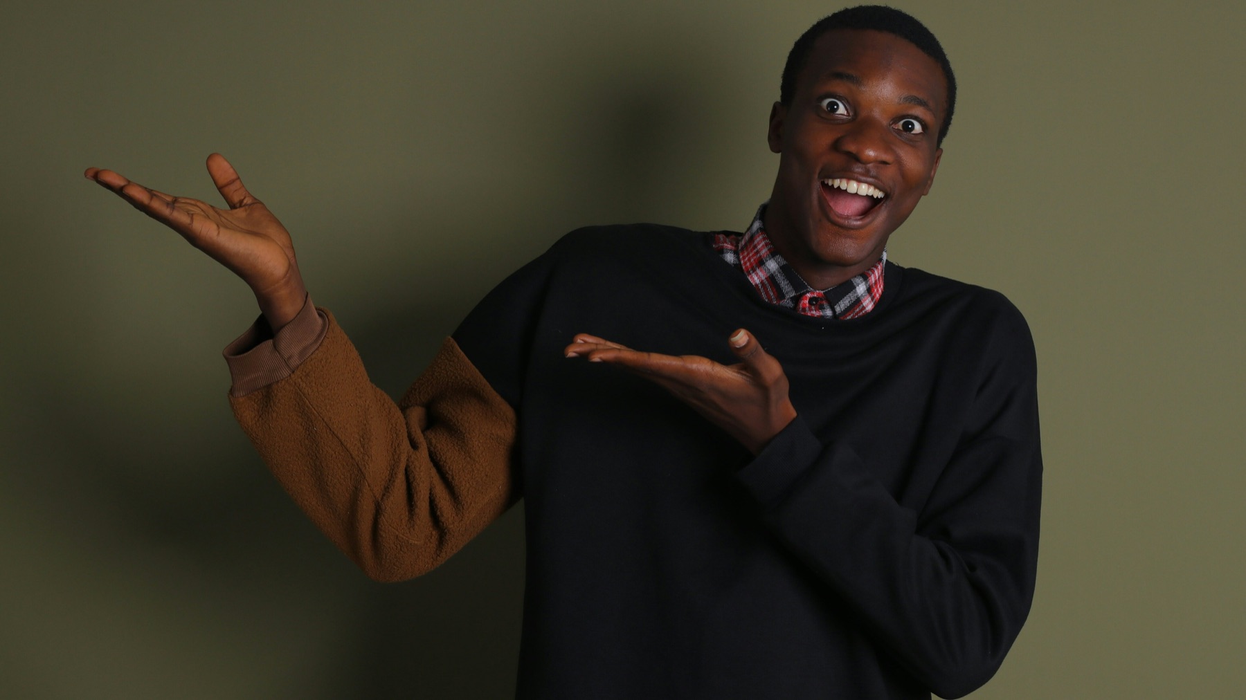 A young man smiling broadly, both open hands raised to one side.